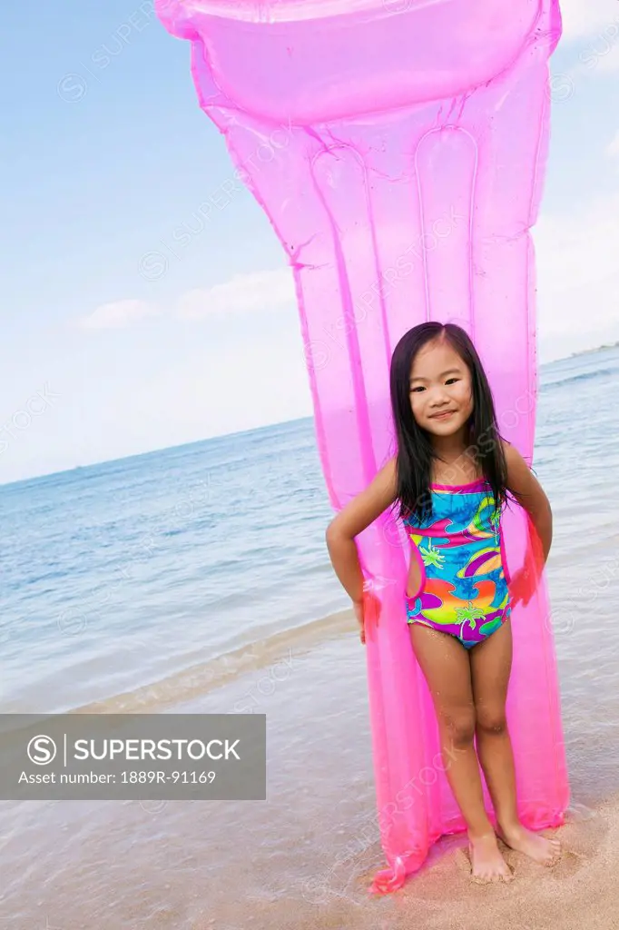 A young girl in a swimsuit holding an inflatable mattress at the water's edge;Honolulu oahu hawaii united states of america