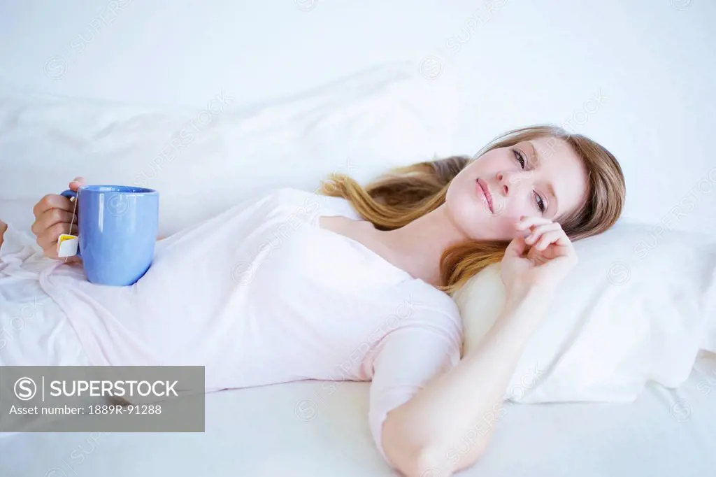 A woman laying in bed with a cup of tea;Kauai hawaii united states of america