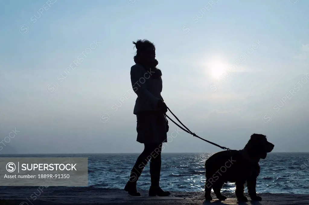Silhouette of a woman and her dog at the water's edge;Ascona ticino switzerland