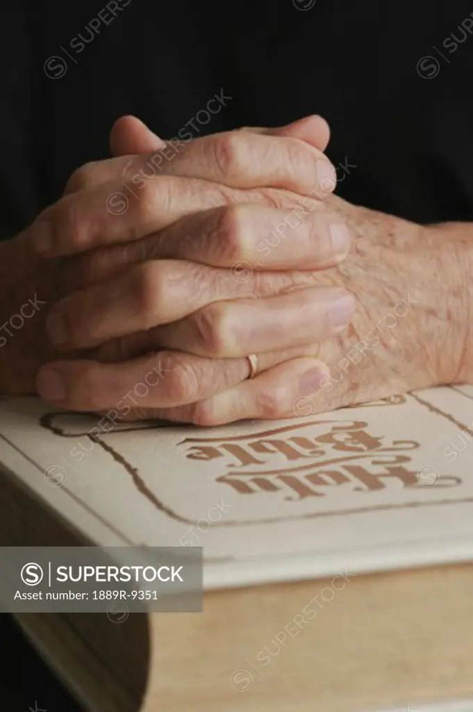 Senior's folded hands on Holy Bible