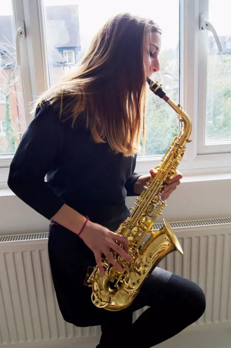 Girl playing saxophone in school uniform; England