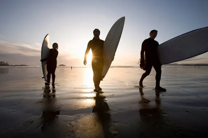 silhouette of three surfers carrying surfboards, chesterman beach tofino vancouver island british columbia canada