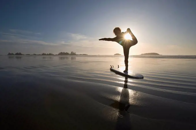 silhouette of female surfer doing bow pulling yoga pose, chesterman beach tofino vancouver island british columbia canada
