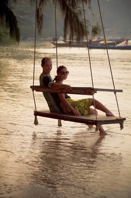 couple sits on beach swing at sunset, koh tao, thailand