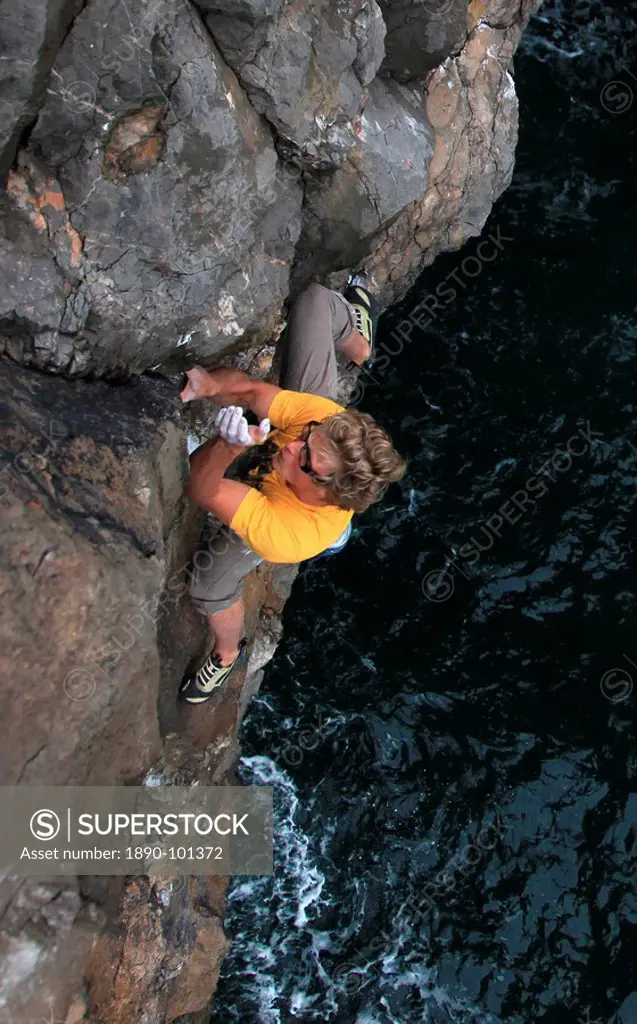 A climber deep water soloing above the sea on the limestone cliffs near St. Govan´s Head, South Pembrokeshire, Pembrokeshire Coast National Park, Wale...