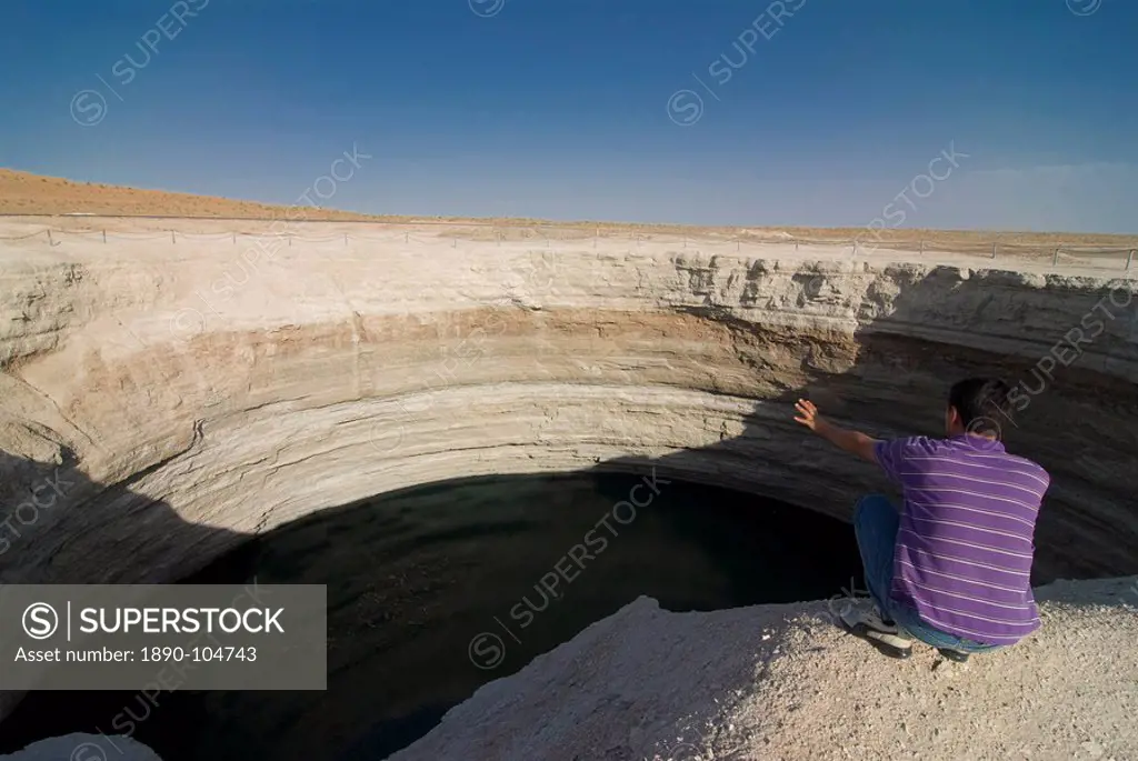 Man sitting on top of a crater filled with water, Karakol desert, Turkmenistan, Central Asia, Asia
