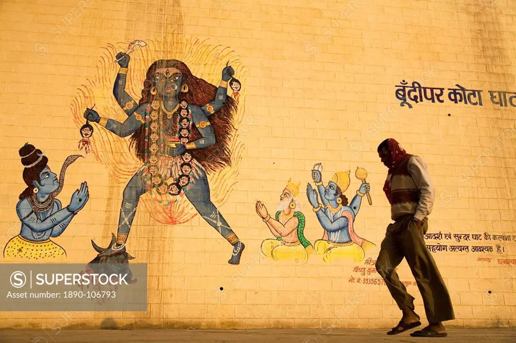 An Indian man walks by a wall painted with images of Hindu deities in Varanasi, Uttar Pradesh, India, Asia
