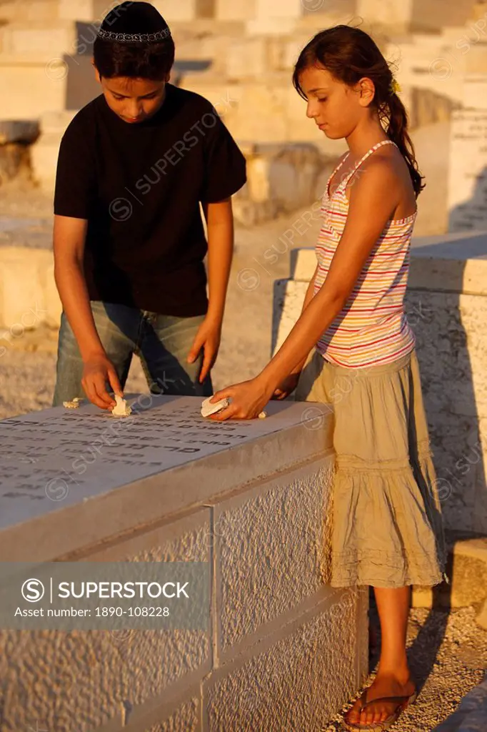 Brother and sister placing stones on a grave in the Mount of Olives Jewish cemetery, Jerusalem, Israel, Middle East