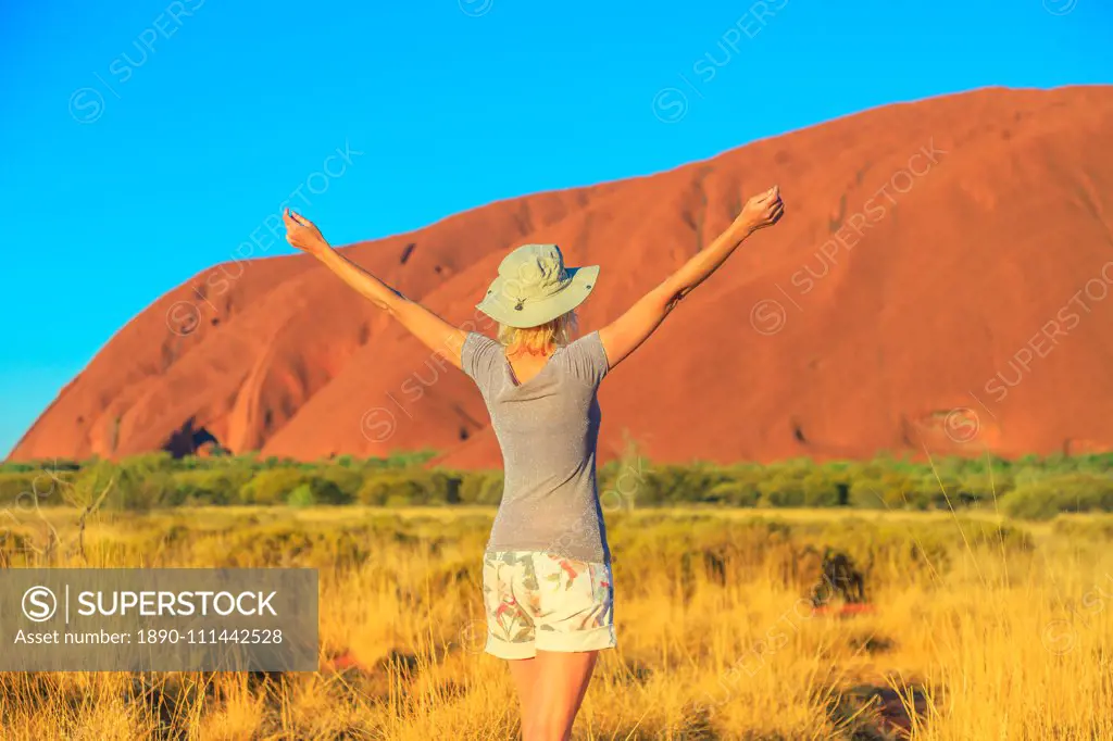 Carefree tourist woman with raised arms enjoys Uluru (Ayers Rock) at sunset in Uluru-Kata Tjuta National Park, UNESCO World Heritage Site, Northern Territory, Australia, Pacific