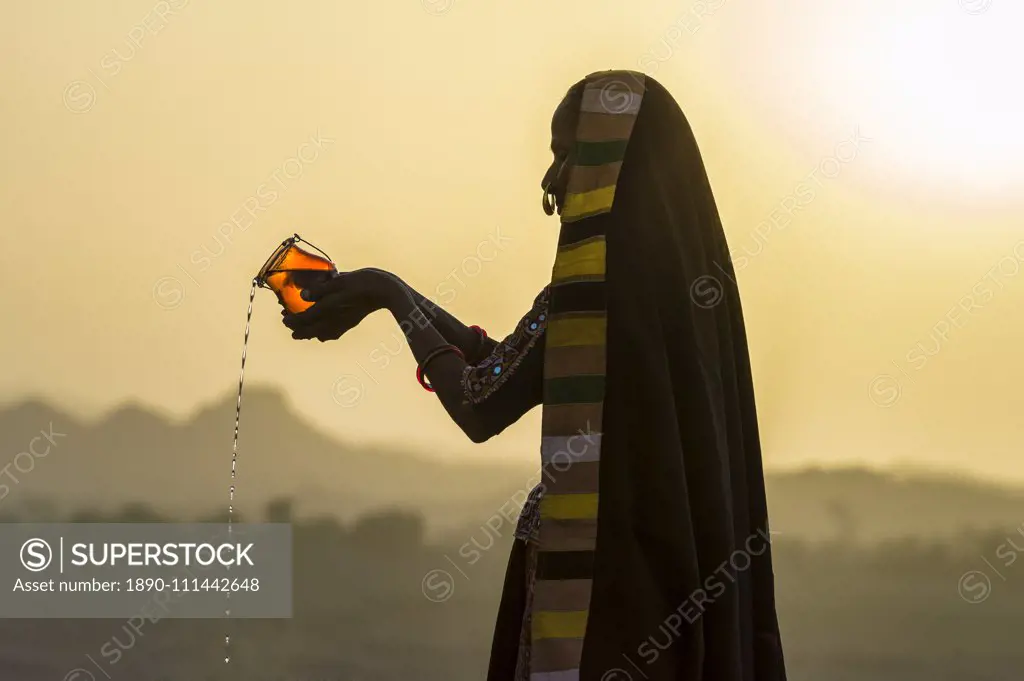 Ahir Woman in traditional colorful cloth pouring water at sunset, Great Rann of Kutch Desert, Gujarat, India, Asia