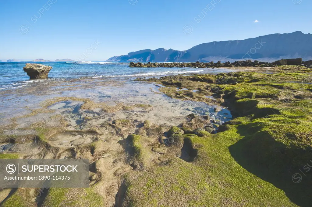 Spectacular 600m volcanic cliffs of the Risco de Famara and Graciosa Island backdrop to the rocky southern shore of the bay at Famara in the north wes...