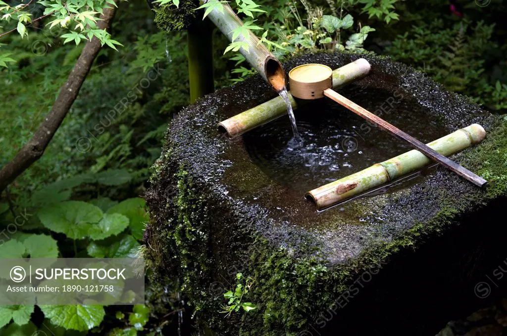 A tsukubai stone water basin with bamboo ladle in a garden at Sanzenin Temple in Ohara, Kyoto, Japan, Asia