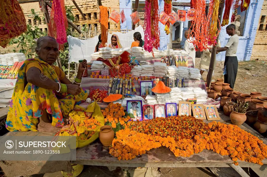 Woman selling marigold mala garlands, pictures of Hindu deities, agarbathi joss sticks and rolimoli temple threads from stall at Sonepur Cattle Fair, ...