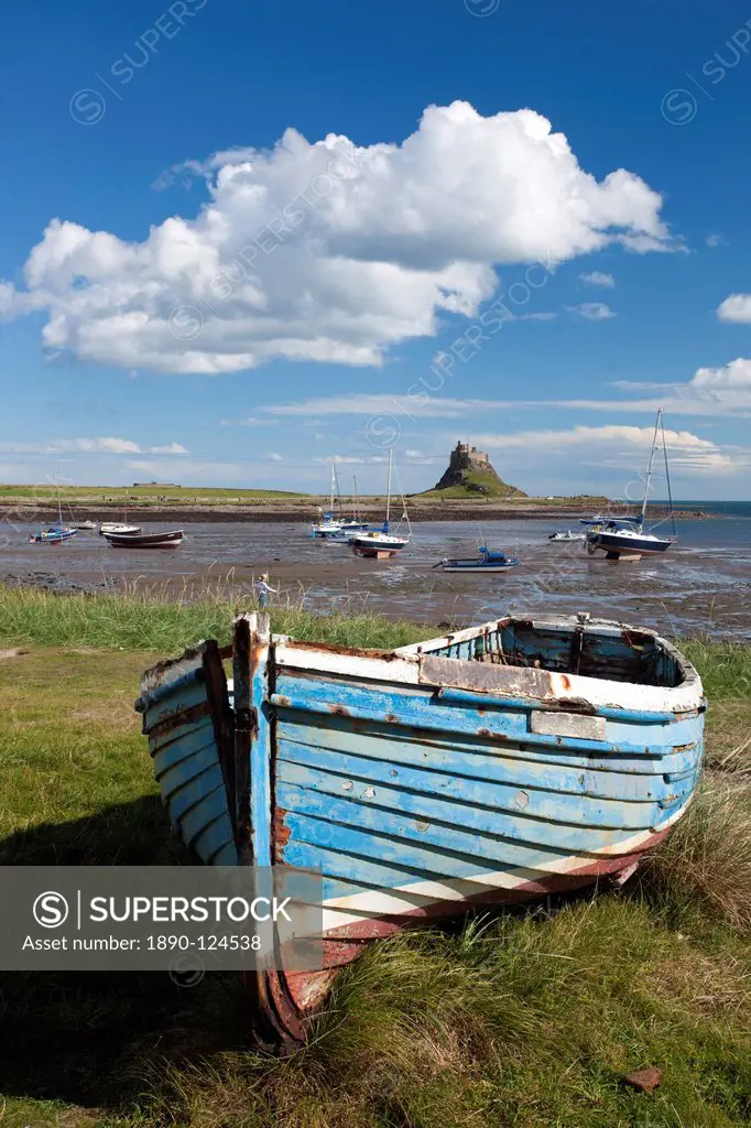Old wooden fishing boat on a grassy bank with Lindisfarne harbour and Lindisfarne Castle in the background, Holy Island Lindisfarne, Northumberland, E...