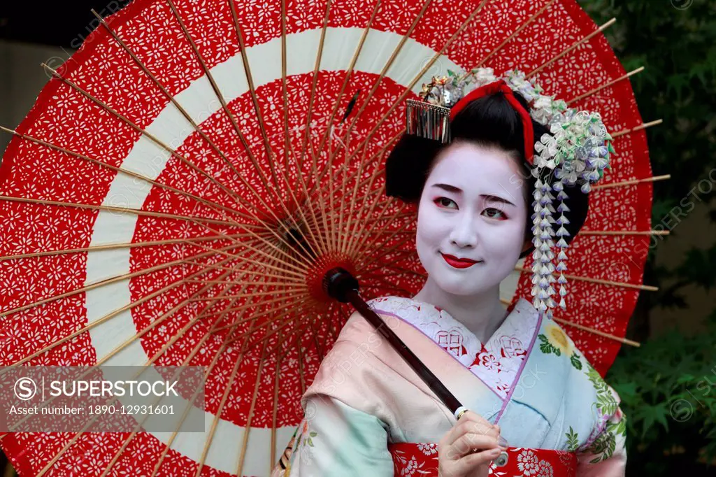 Portrait of smiling geisha in floral robes with red umbrella in summer, Kyoto, Japan, Asia