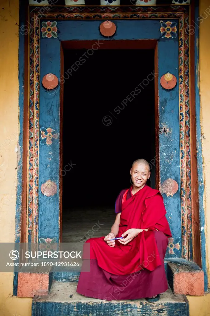 Young monk sitting in an ornate doorway, Punakha, Bhutan, Asia
