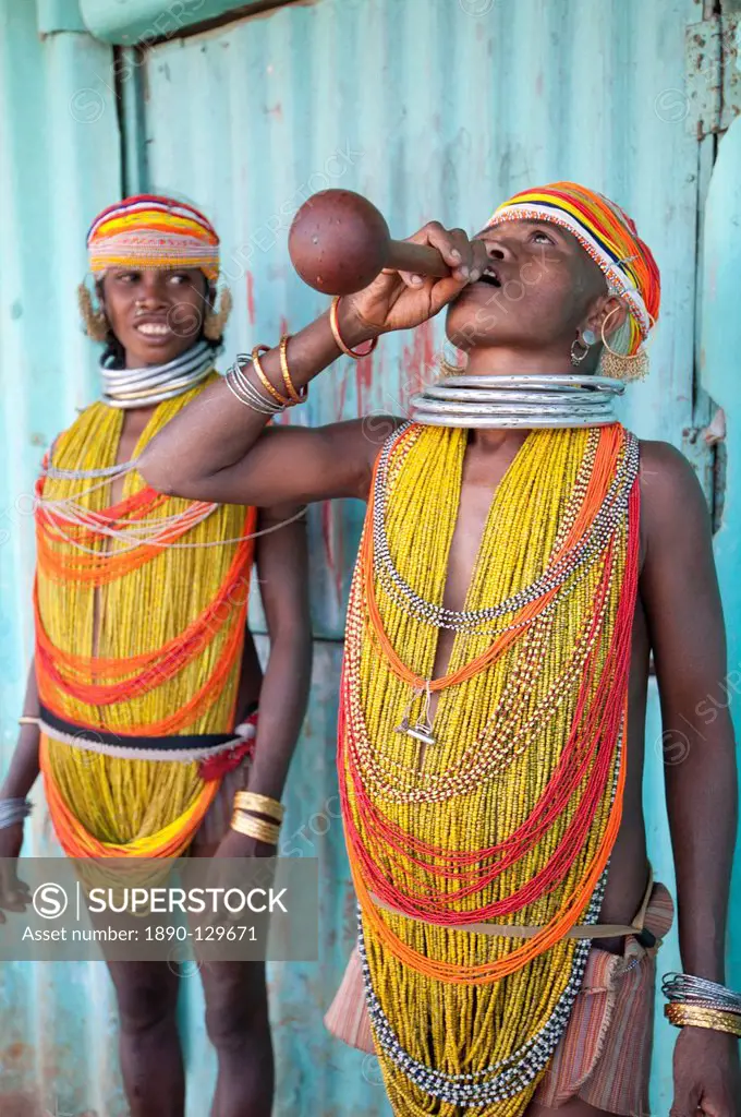 Two Bonda tribeswomen wearing traditional beads with beaded caps and metal necklaces drinking village alcohol from gourd vessel, Rayagader, Orissa, In...