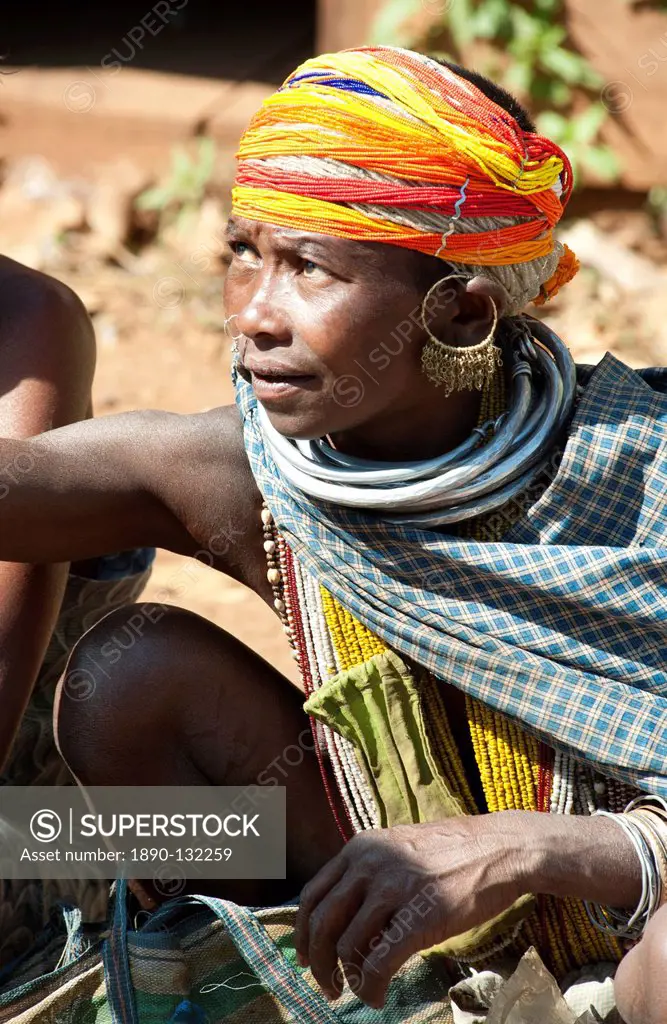 Bonda tribeswoman in traditional dress with beaded cap, large earrings and metal necklaces selling vegetables at weekly market, Rayagader, Orissa, Ind...