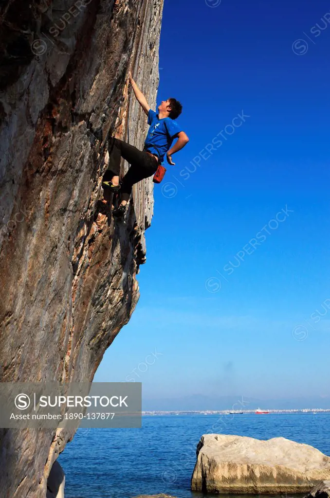 A climber tackles a difficult route on the limestone sea cliffs of Akyalar, with the city of Antayla in the distance, Anatolia, Turkey, Asia Minor, Eu...
