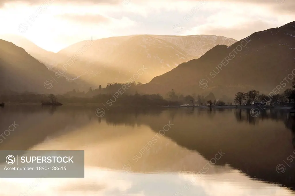 Morning sunlight bursting through clouds over fells with reflections in Lake Ullswater, near Glenridding Village, Lake District National Park, Cumbria...