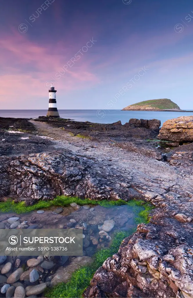 Twilight on the rocky Anglesey coast looking towards Penmon Point Lighthouse and Puffin Island, Anglesey, North Wales, Wales, United Kingdom, Europe