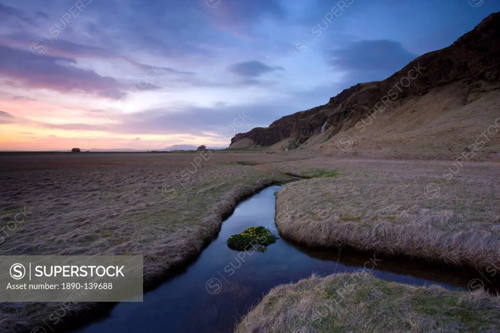 Stream meandering into the distance and reflecting colours in the twilight sky, near Hella, South Iceland, Iceland, Polar Regions