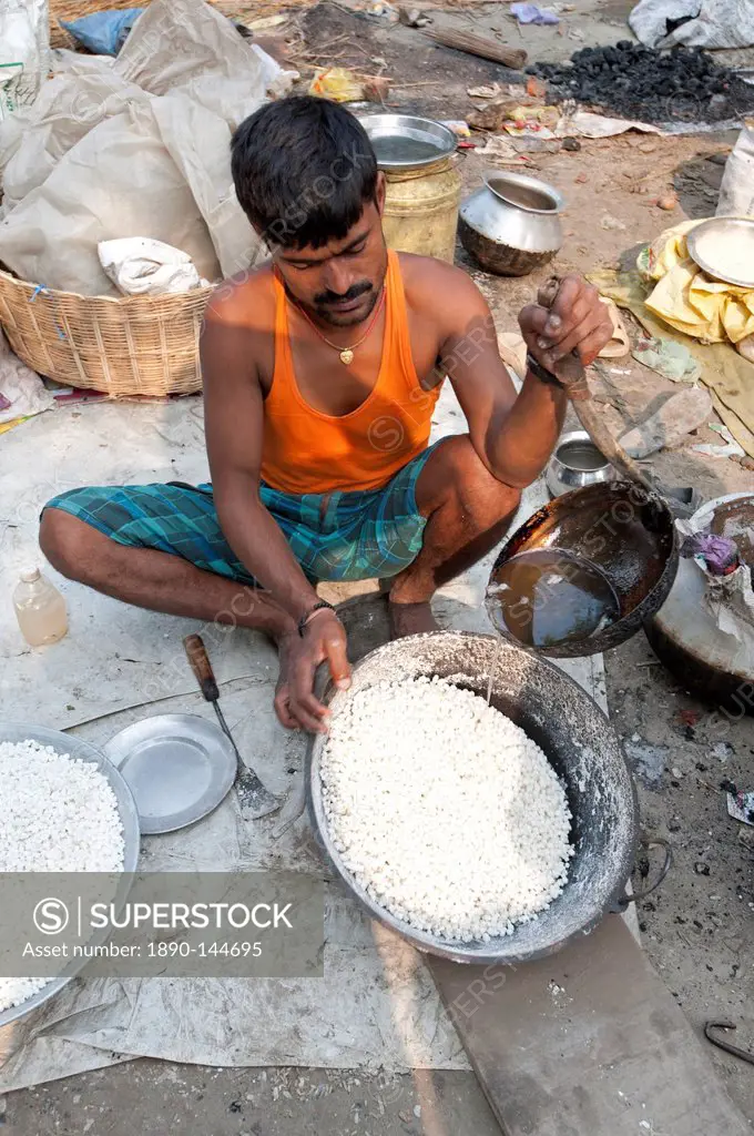 Man in vest and dhoti pouring sugar syrup onto bowl of puffed rice to make prasad, Sonepur Cattle Fair, Bihar, India, Asia