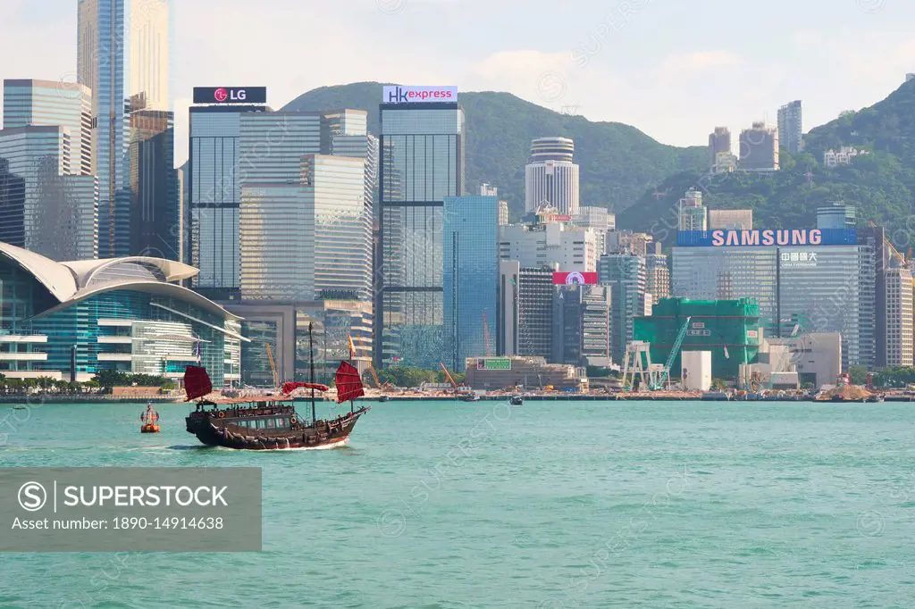 Traditional junk boat on Victoria Harbour with city skyline behind, Hong Kong, China, Asia
