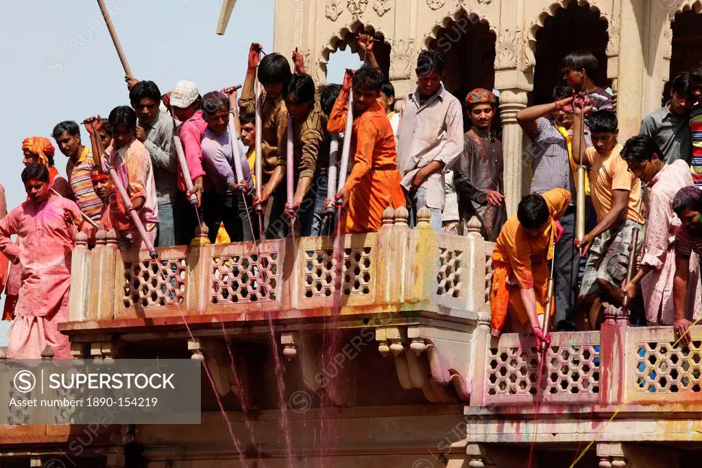Young men celebrating Holi festival by splashing colored fluids on temple visitors, Nandgaon, Uttar Pradesh, India, Asia
