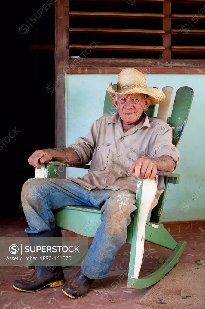 Tobacco farmer wearing straw hat and Wellington boots, on a rocking chair outside his house, Vinales, Pinar Del Rio, Cuba, West Indies, Central Americ...