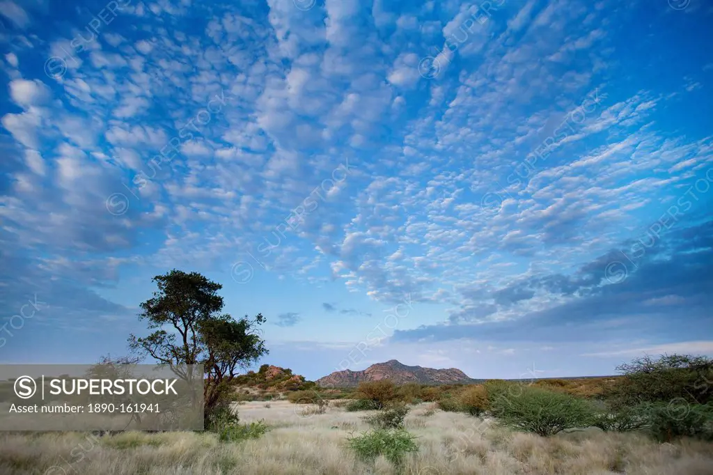 Early morning view across barren landscape towards sandstone mountains beneath dramatic sky, near Spitzkoppe, Namibia, Africa