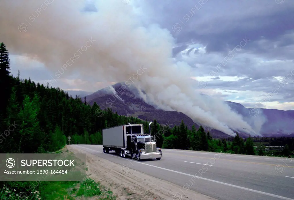 Articulated truck driving past the smoke of a forest fire in Canada