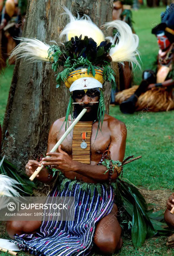 Bearded tribesman wearing feathered headdress and playing a pipe during a gathering of tribes at Mount Hagen in Papua New Guinea