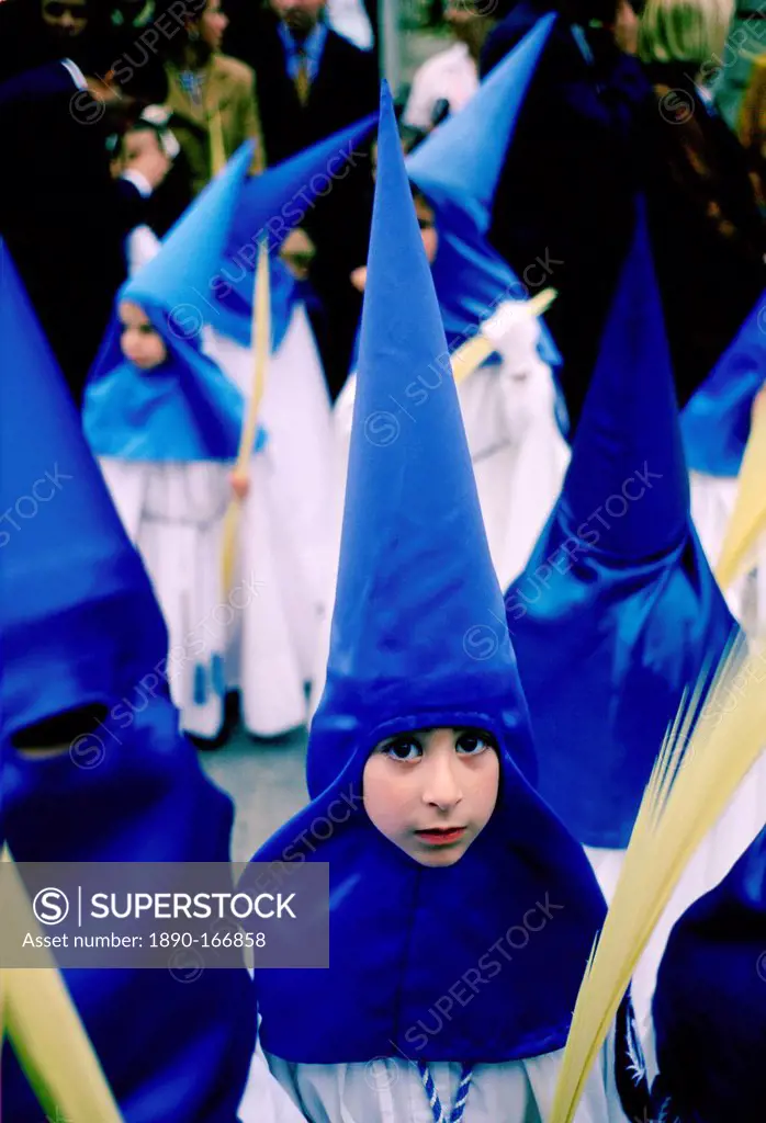 Young girl staring out from her blue silk hooded costume while taking part in the Semana Santa parade for Holy Week in Seville, Spain (Sevilla). They ...
