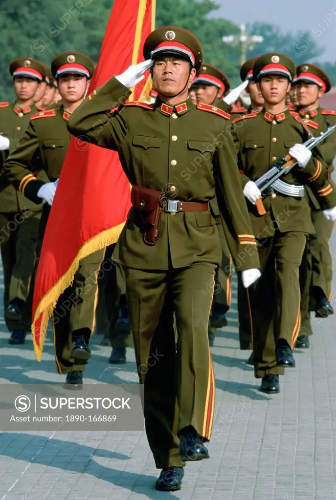Soldiers salute while marching in Tiananmen Square with a red flag in Beijing (Peking), China