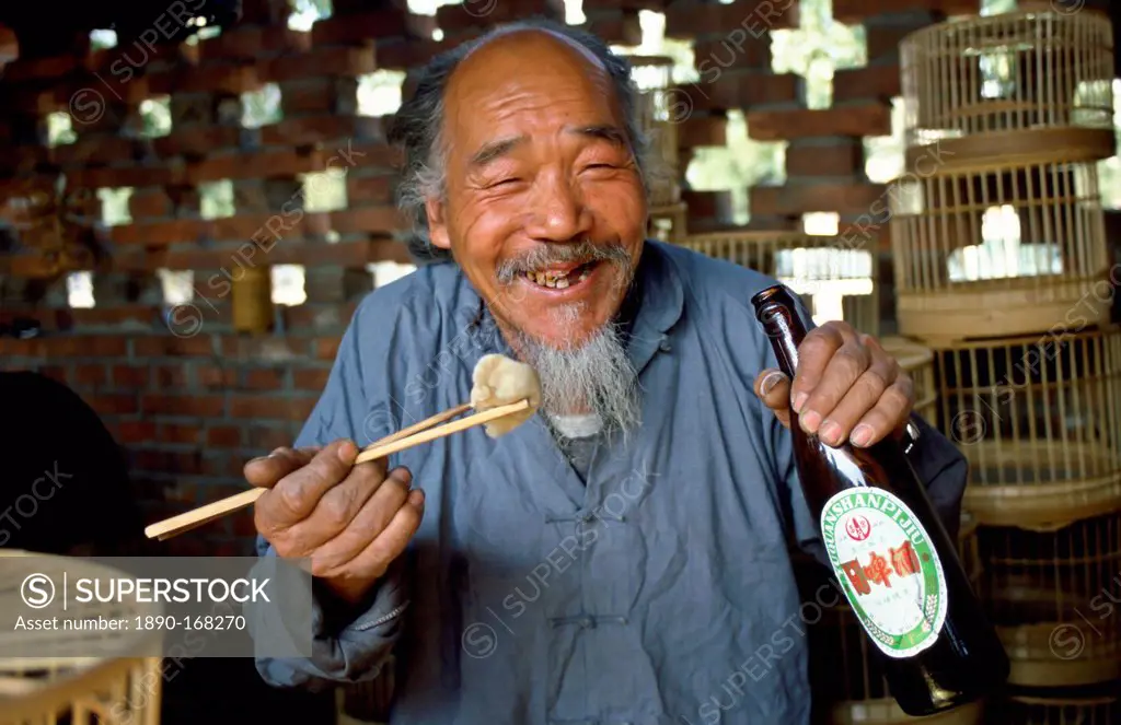Market trader selling bird cages stops for a beer and his lunch using chopsticksduring a break in Peking (Beijing) China