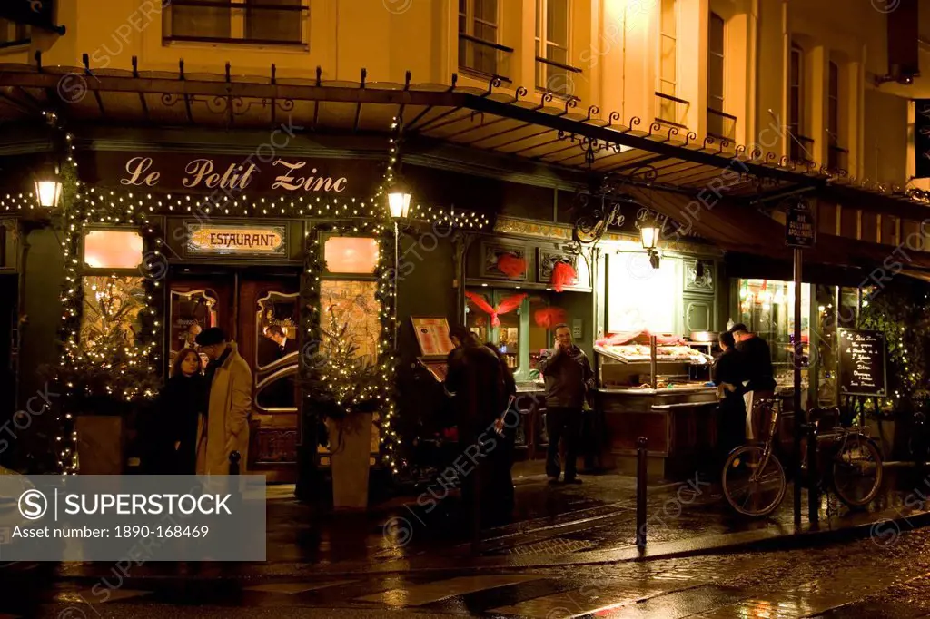 People shelter from rain at night on street corner outside traditional Le Petit Zinc Restaurant, Left Bank, Paris, France