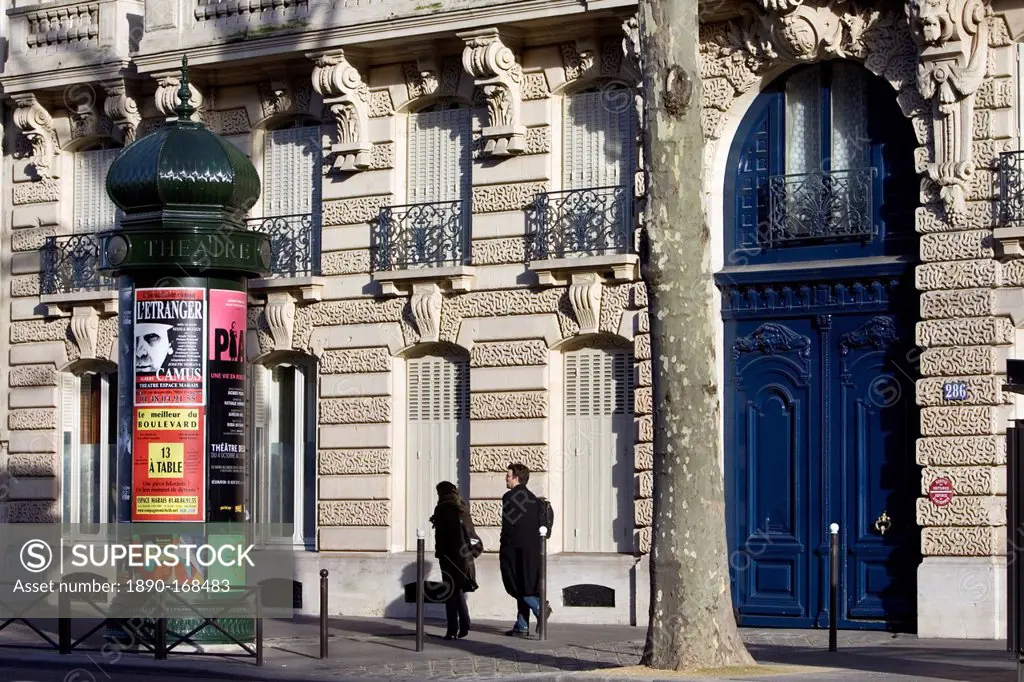 Couple walk past obelisk advertising theatre productions in Parisian street, Boulevard St Germain, Latin Quarter, France