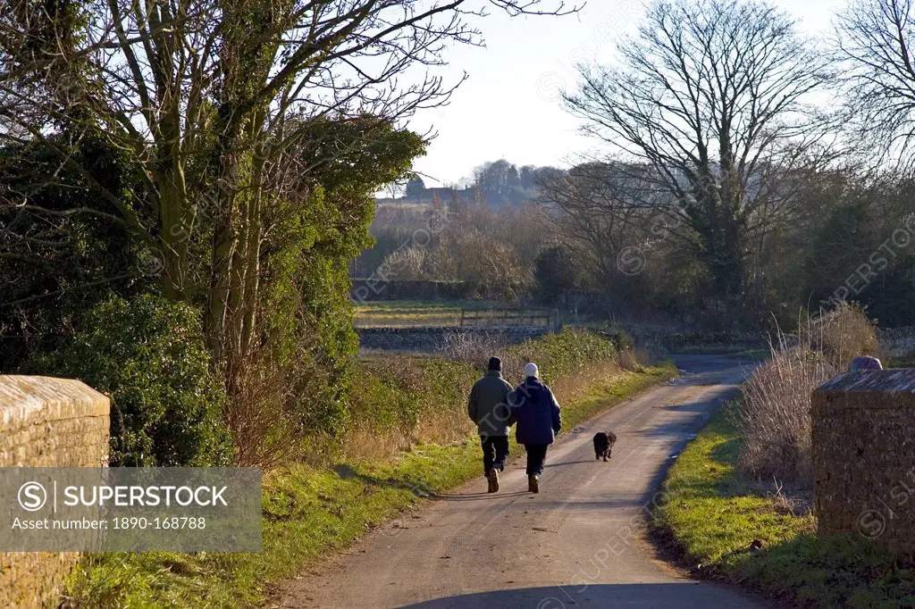 Couple walk their dog on a country lane in Asthall Leigh, Oxfordshire, United Kingdom