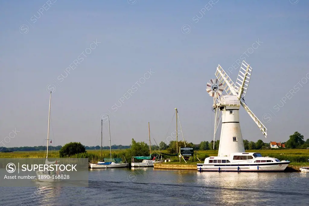 Sailing boats and river cruisers pass windmill on Norfolk Broads, United Kingdom