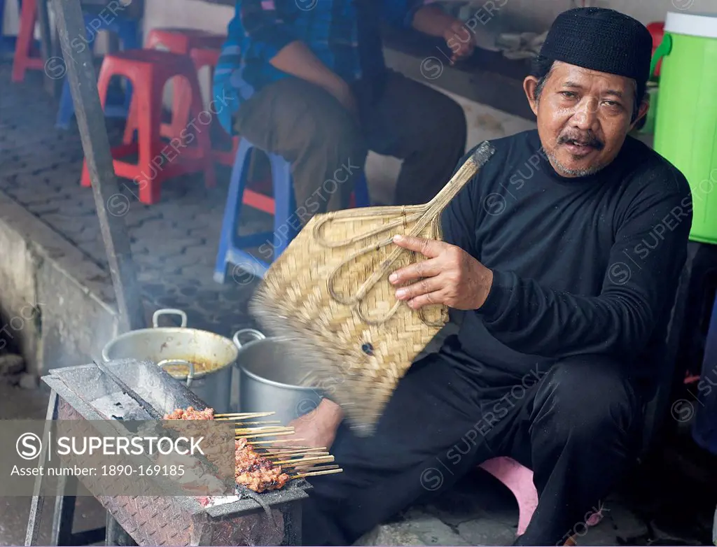 Muslim man in the market cooking chicken satay, fanning the charcoal with a palm leaf fan, Solo, Java, Indonesia, Southeast Asia, Asia