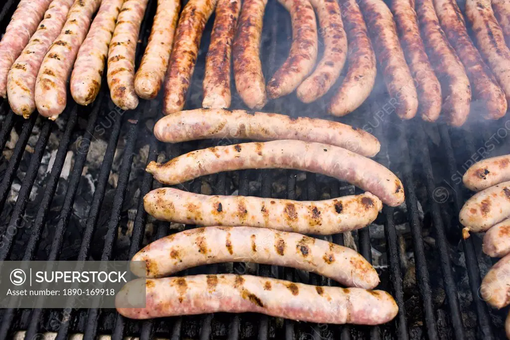 Barbecued sausages saucissons being cooked on griddle for sale as snack food at farmers market in Normandy, France