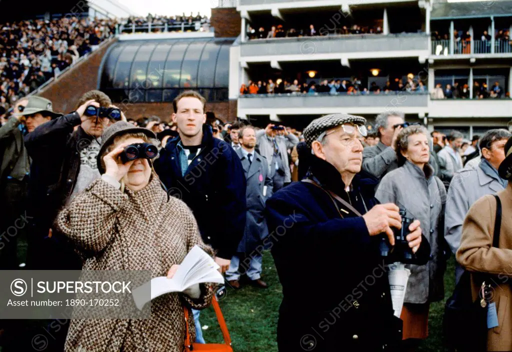 Spectactors with binoculars in front of grandstand at Cheltenham Racecourse for the National Hunt Festival of Racing, UK