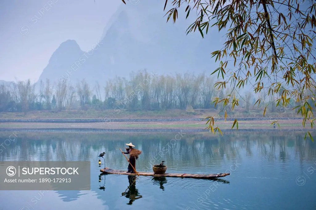 Fisherman in Suoyi coat and coolie hat fishes with cormorants on Li River near Guilin, China