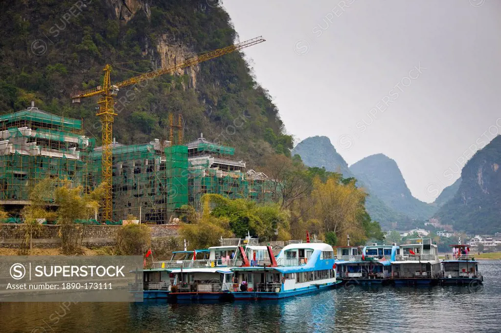 Tourist boats moored on the Li River at Yangshuo by a hotel construction site, China