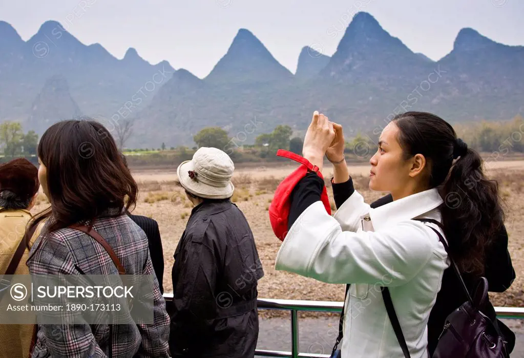 Tourist take photographs as she travels by boat along Li River between Guilin and Yangshuo, China