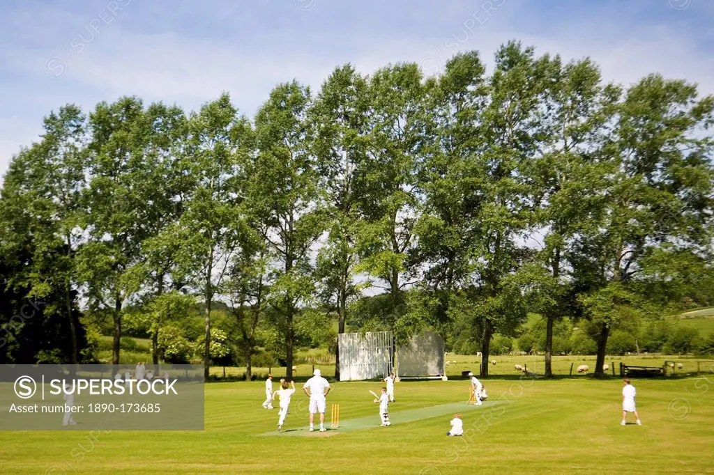 Children play cricket on village pitch, Swinbrook, The Cotswolds, England, United Kingdom