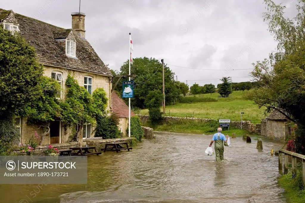 Man wades through flood water in Swinbrook, Oxfordshire, England, United Kingdom