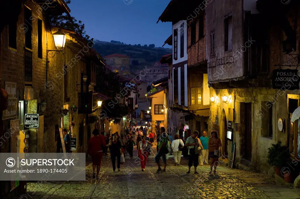 Tourists stroll at night past medieval buildings on cobbled street of Calle Del Canton in Santillana del Mar, Cantabria, Spain