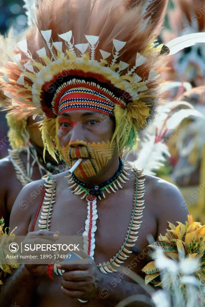 Tribesman smoking a cigarette while wearing face paints and feathered headdress during a gathering of tribes at Mount Hagen in Papua New Guinea